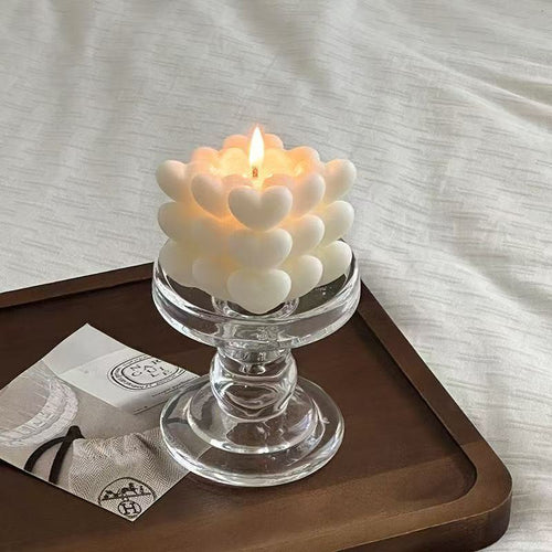 Candle with heart-shaped design in a glass holder on a wooden tray.